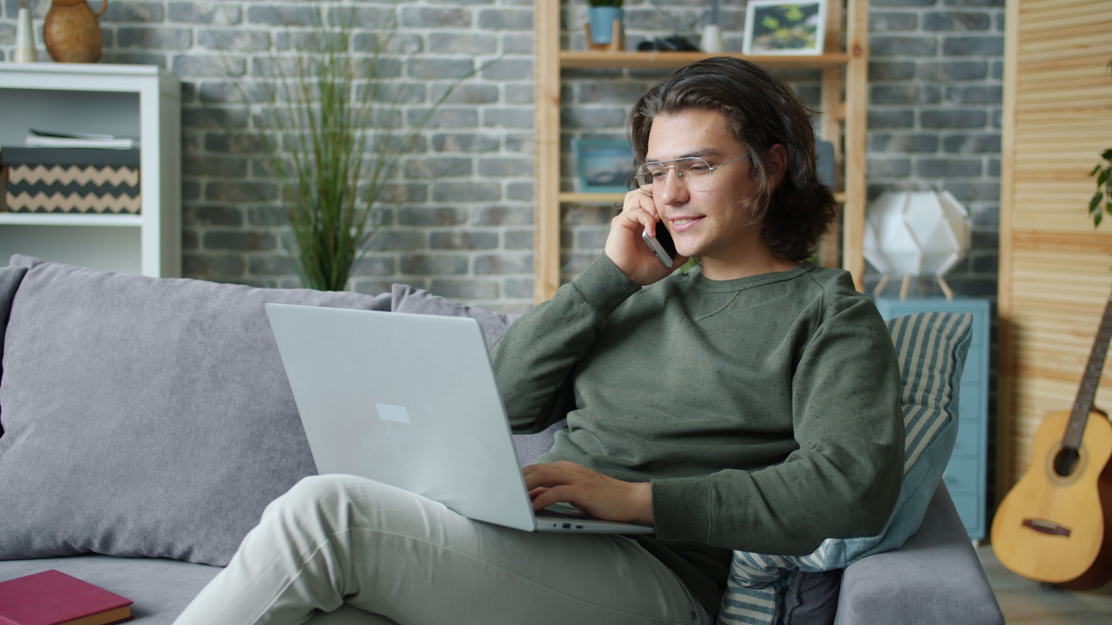 Gastgeber sitzt entspannt mit Laptop auf dem Sofa und telefoniert, während REPLAI die Gästefragen beantwortet
